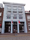 Huis met brede, gebosseerd witgepleisterde lijstgevel. Moderne etalages